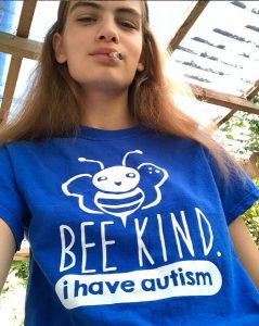 Nina Marker poserer med en blå t-shirt. På T-shirten er der en hvid bi, og under den står der: Bee kind, I have autism.